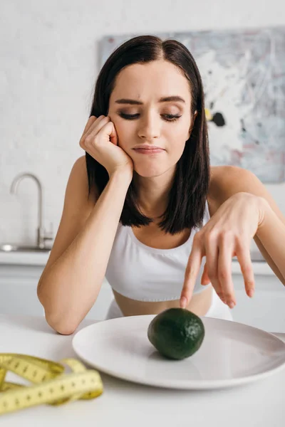 Selective Focus Thoughtful Sportswoman Looking Avocado Measuring Tape Kitchen Table — 스톡 사진