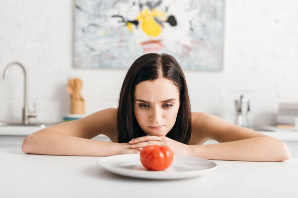 Pensive girl looking at ripe tomato on kitchen table 