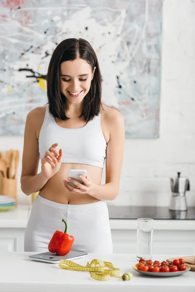 Glimlachende Sportvrouw Met Smartphone Buurt Van Meetlint Groenten Schalen Keukentafel — Stockfoto