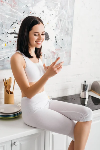 Smiling Sportswoman Holding Glass Water Using Smartphone Kitchen Table — Stock Photo, Image