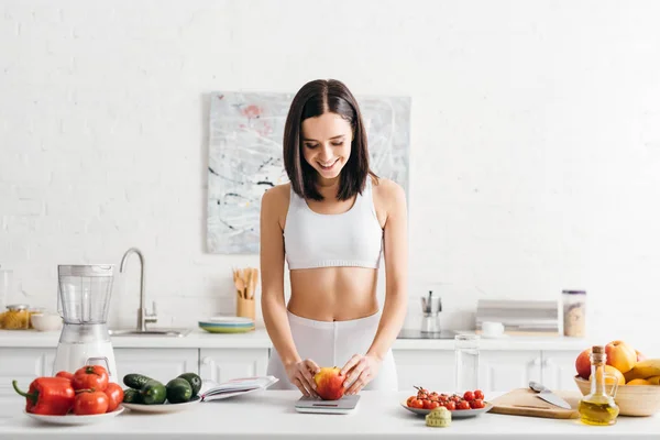 Beautiful Smiling Sportswoman Weighing Apple Vegetables Measuring Tape Notebook Kitchen — Stockfoto