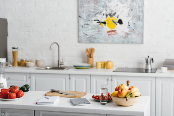 Fresh vegetables, fruits with glass of water and notebook on kitchen table, calorie counting diet