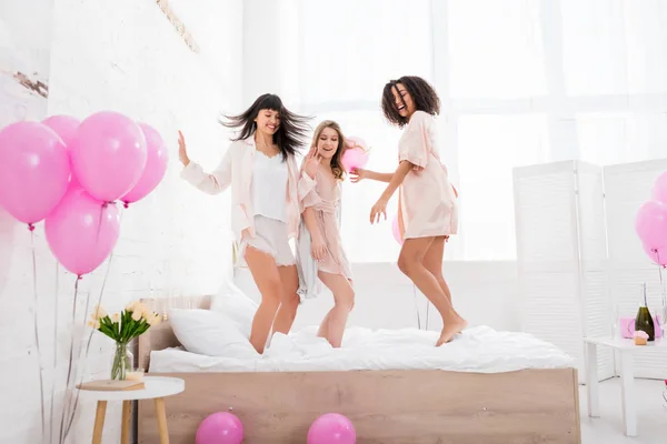 Emotional Multiethnic Girlfriends Jumping Bed Pink Balloons — Stock Photo, Image