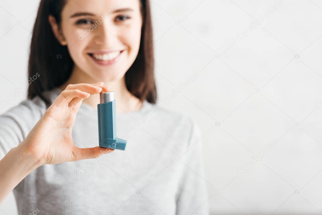 Selective focus of girl holding inhaler and smiling at camera on white background