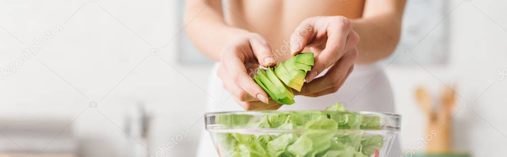 Cropped view of fit woman cooking salad with juicy avocado in kitchen, panoramic shot