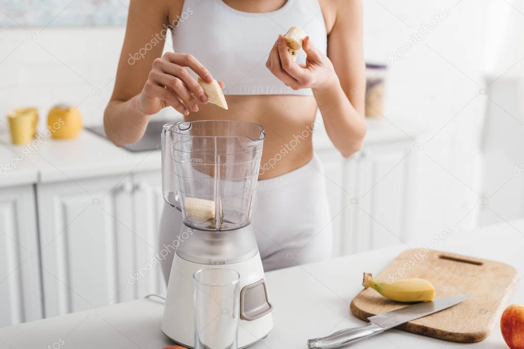 Cropped view of sportswoman preparing banana smoothie on kitchen table
