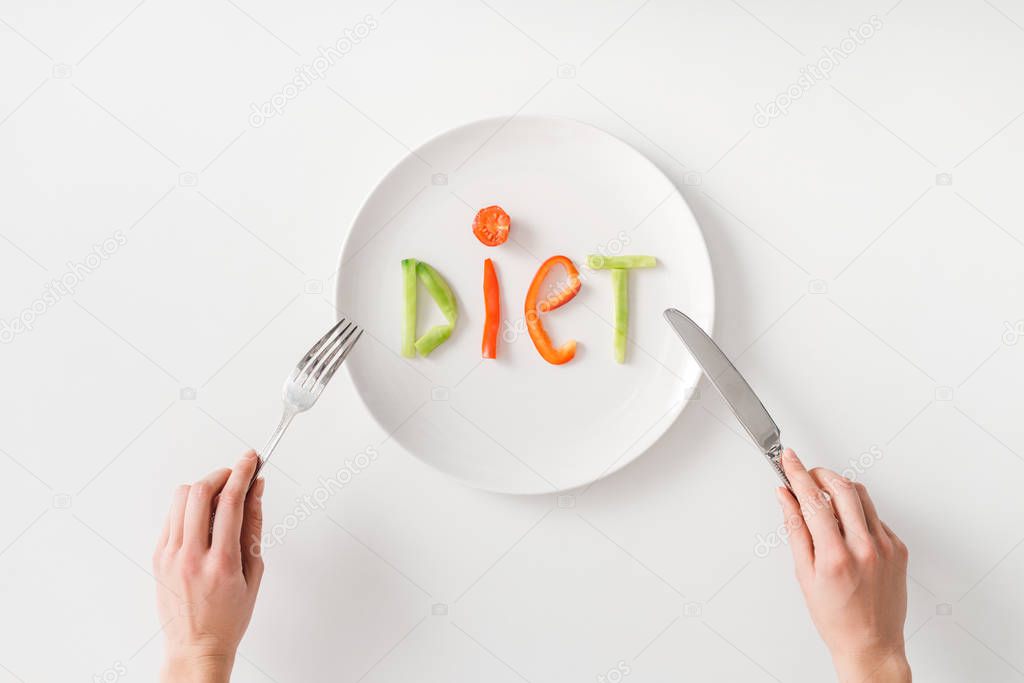 Top view of woman with cutlery and diet lettering from vegetable slices on plate on white background