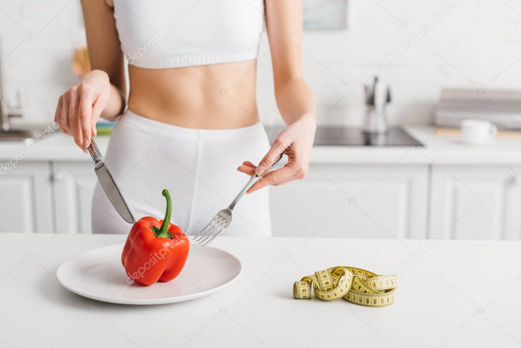 Cropped view of sportswoman with cutlery near bell pepper and measuring tape on table