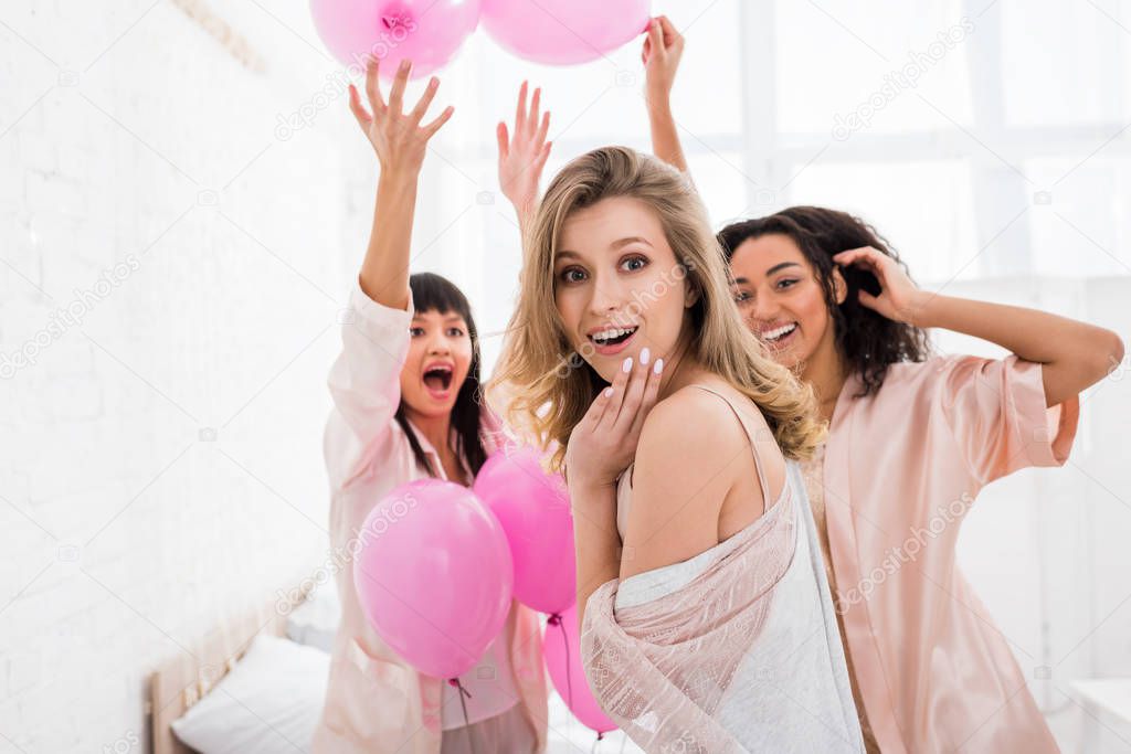 excited multicultural girls having fun with pink balloons on pajama party