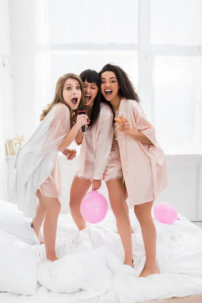 Excited Multicultural Girls Holding Champagne Singing Microphone Pajama Party — Stock Photo, Image