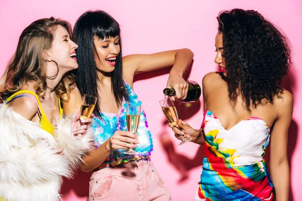 Emotional Multicultural Girlfriends Pouring Champagne Bottle Glasses Pink — Stock Photo, Image