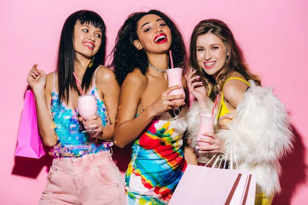 Возбужденные Модные Мультиэтнические Девушки Позируют Молочными Коктейлями Сумками Покупок Розовом — стоковое фото