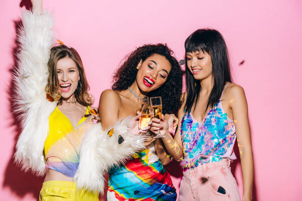 веселые мультикультурные девушки веселятся с бокалами шампанского на розовом с конфетти
