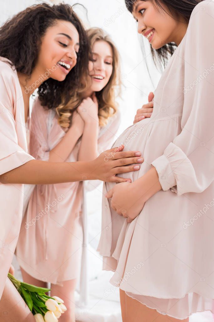 multicultural girlfriends touching belly of young pregnant woman on baby shower 