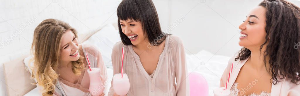 panoramic shot of multicultural girlfriends and laughing pregnant woman holding glasses with milkshakes on baby shower 
