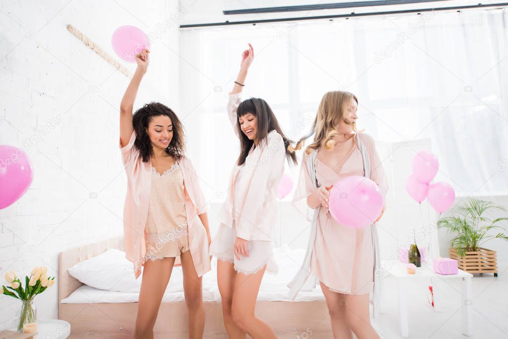 happy multicultural girls dancing with pink balloons in bedroom