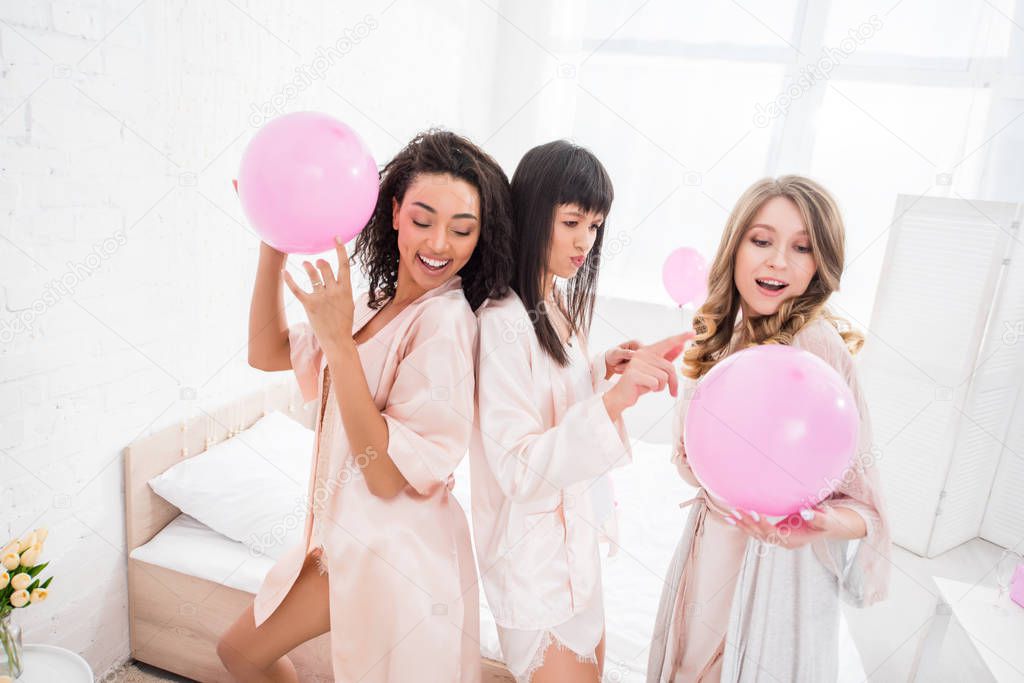 smiling multicultural girls dancing with pink balloons on bachelorette party
