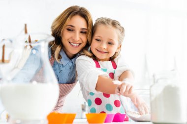 Güzel anne ve kızın seçici odak noktası. Mutfakta süt ve un da dahil olmak üzere içerikli kekler hazırlıyorlar.