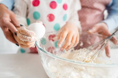 Çocuğun yumurtayı çanağın yanında tutması ve annenle lezzetli kekler için hamur yoğurması seçici bir odak noktası.