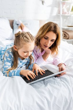 Çekici anne ve gülümseyen kız yatak odasında dizüstü bilgisayar kullanıyor. 