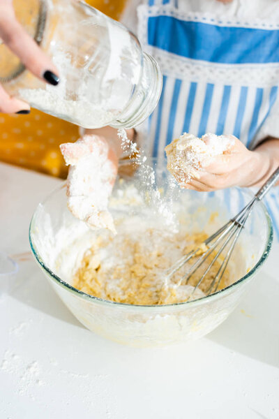 cropped view of mother adding flour to bowl and daughter cooking dough 