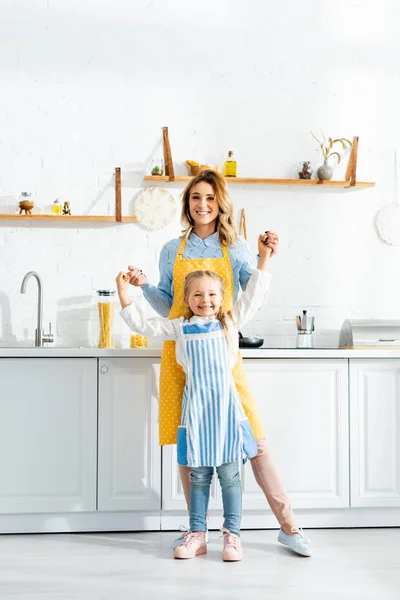 Sonriente Madre Cogida Mano Con Hija Mirando Cámara Cocina —  Fotos de Stock