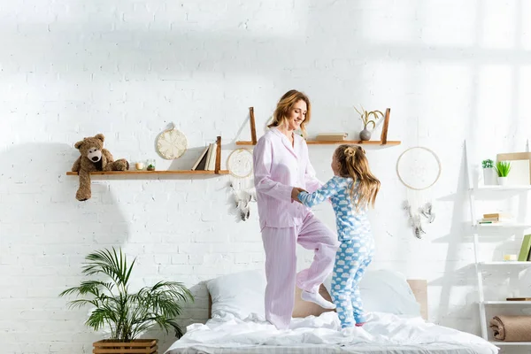 笑着的母亲和女儿牵着手 跳上了床 — 图库照片