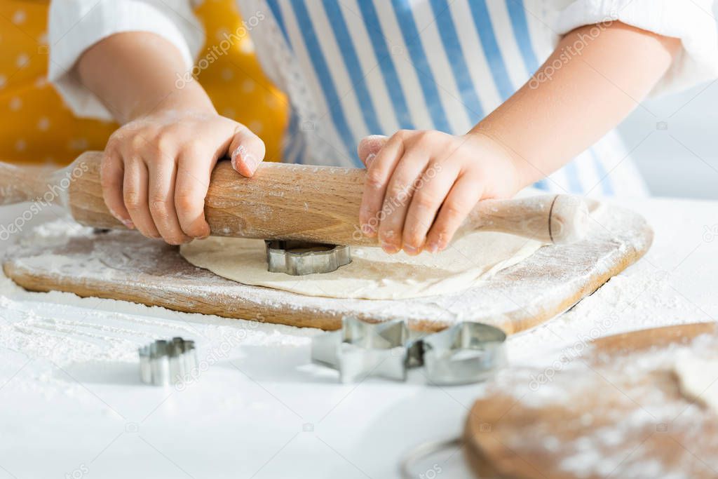 cropped view of kid rolling dough with rolling pin