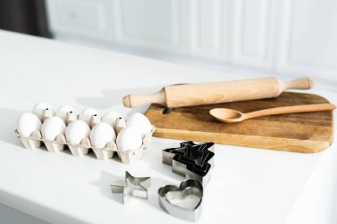 Yumurta, kesme tahtası, kaşık, hamur kalıpları ve masa üzerindeki merdane. 