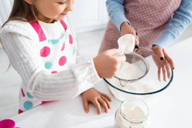 cropped view of mother holding sieve and smiling daughter sifting flour  clipart