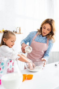 Anne kâseye un ekliyor ve gülümseyen kız mutfakta yemek pişiriyor. 