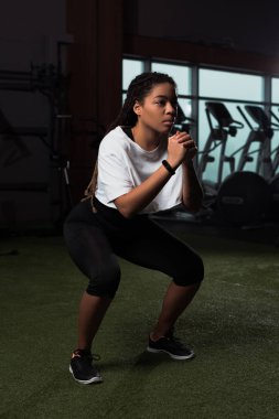 Afrikalı Amerikalı çekici kadın ellerini sıkıyor ve spor salonunda çömeliyor.