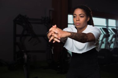 Selective focus of african american attractive woman clenching hands and training in gym clipart