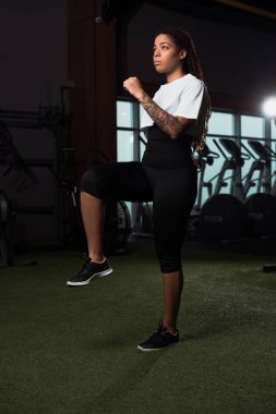 Afrika kökenli Amerikalı bir kadın spor salonunda ısınırken bacağını ve elini kaldırıyor.