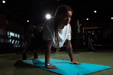Güzel Afrikalı Amerikalı kadın spor salonundaki spor paspasın üzerinde duruyor.