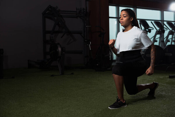 African american woman doing lunges in gym