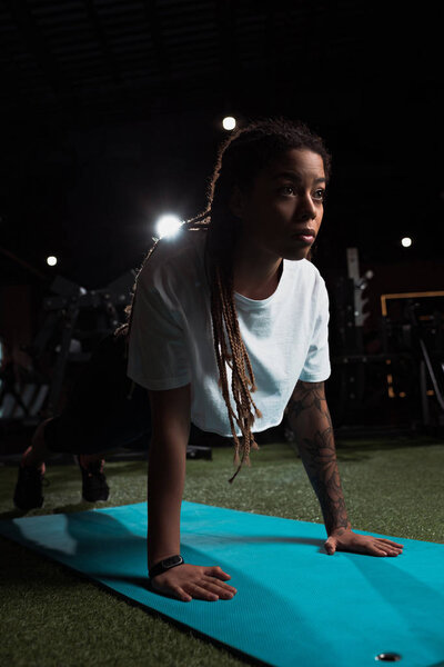 African american woman standing in plank on fitness mat in gym