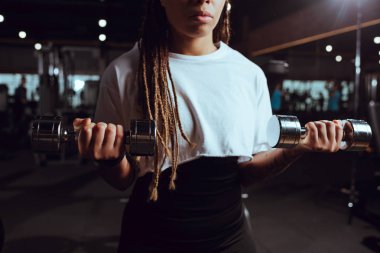 Cropped view of african american woman lifting dumbbells clipart