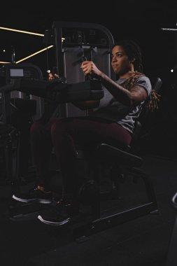 Dövmeli Afrikalı Amerikalı kız Rastalı saçlarıyla spor makinesinde çalışıyor.