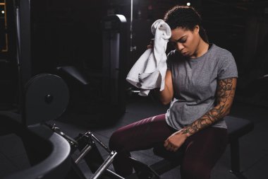 tired african american girl with tattoo wiping sweat with towel 