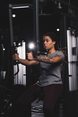 sportive african american girl with tattoo training on gym machine 