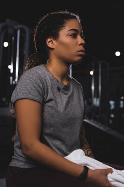 pensive african american sportswoman holding towel in gym 