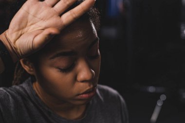 african american girl with closed eyes wiping sweat with hand
