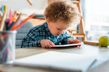 Dijital tablet kullanan sevimli ve kıvırcık çocuğun seçici odağı 