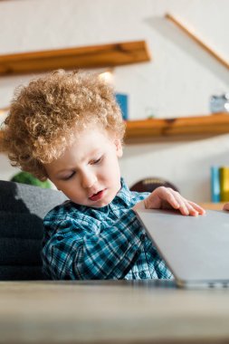 Laptop kullanan zeki ve kıvırcık çocuğun seçici odağı