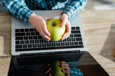 Bilgisayarın yanında elinde taze elma tutan çocuğun boş ekranlı görüntüsü. 