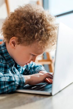 Laptop klavyesinde yazan kıvırcık çocuğun seçici odağı 