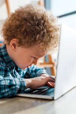 selective focus of curly kid typing on laptop keyboard  clipart
