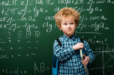 smart kid standing with book near chalkboard with mathematical formulas  clipart