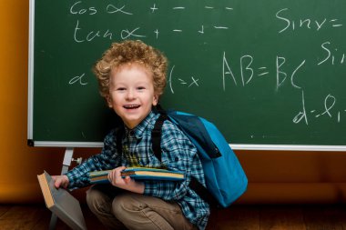 Matematiksel formüllerle kara tahtanın yanında kitap tutarken gülen mutlu çocuk. 